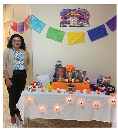 ► Dr. Cynthia Pena stands by an ofrenda, a type of altar in a home used to celebrate and remember the passing of a loved one. Ofrendas are made to honor those people during El Dia de los Muertos, or Day of the Dead. Kimberly Lippencott/WDN